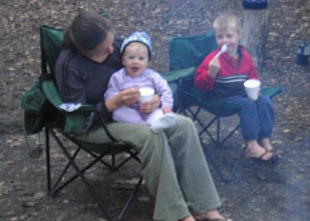 Mom feeding toddler girl ice cream, young boy eating ice cream next to them.