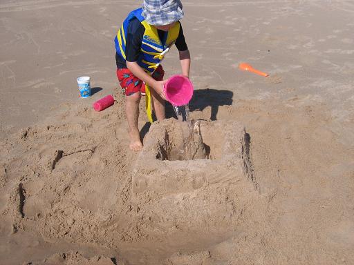 Young boy pouring water into a sand castle