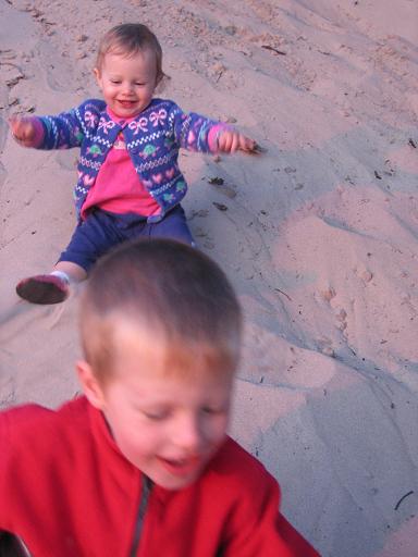 Toddler girl and young boy sliding in the sand.