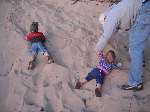 Young boy and toddler girl laying in the sand. 