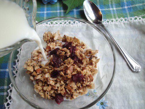Pouring milk into a glass bowl of grain-free homemade granola