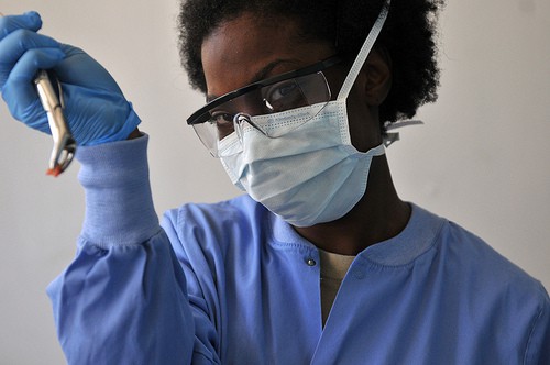 A dental professional in blue scrubs and a surgical mask holding an extracted tooth with a dental tool