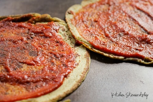 2 cooked chickpea pizza crusts topped with tomato sauce 