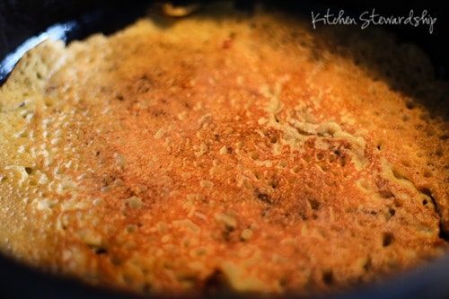 Chickpea flour pizza crust that has just been flipped in a cast iron pan. The chickpea pizza crust is golden brown.