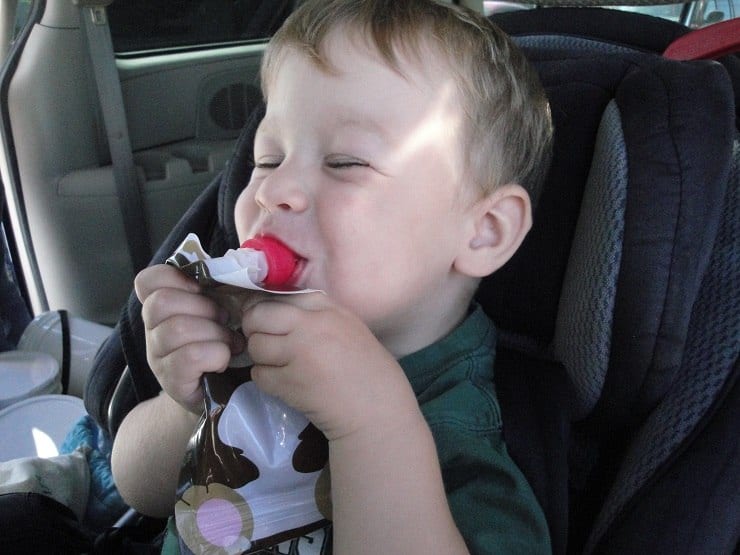 Toddler with Squooshi reusable food pouch in the car
