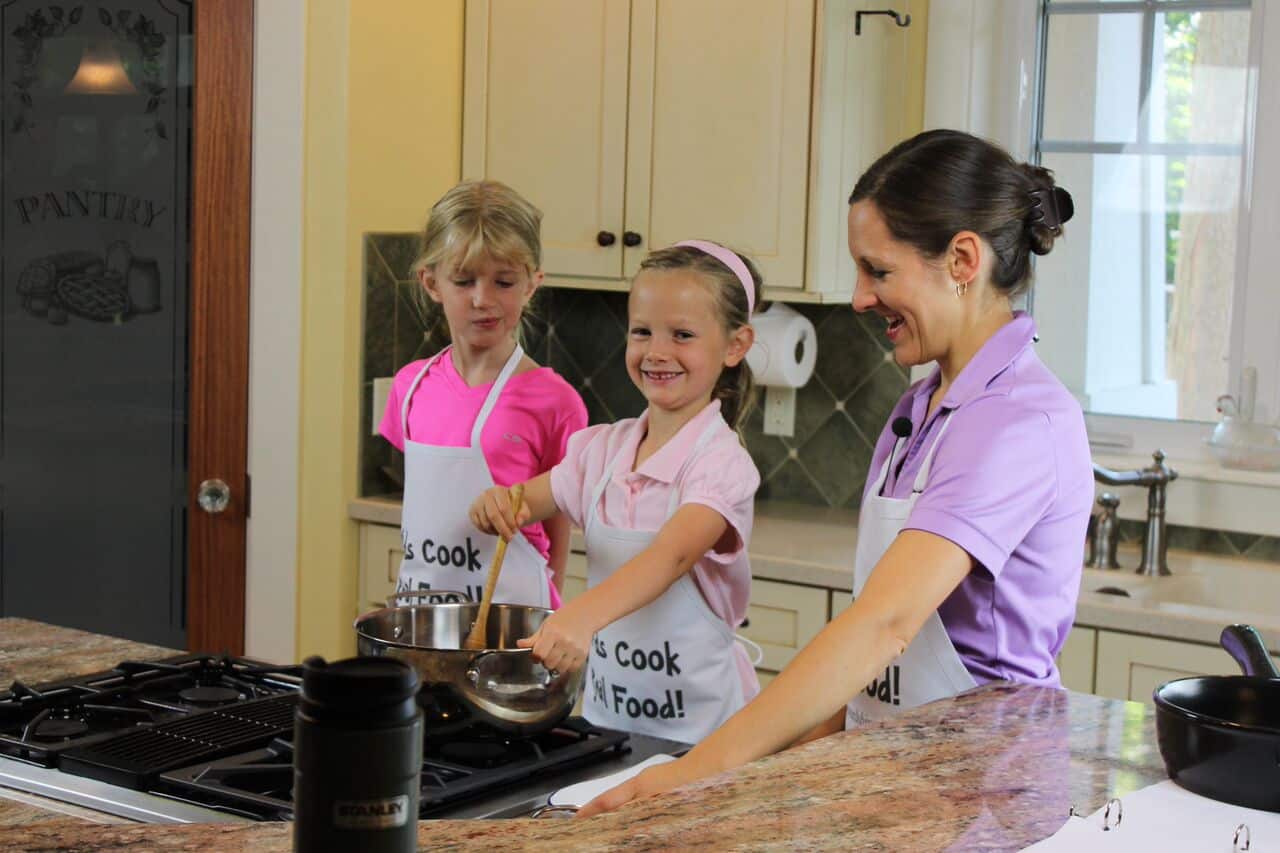 child cooking at a stove with parent and friend
