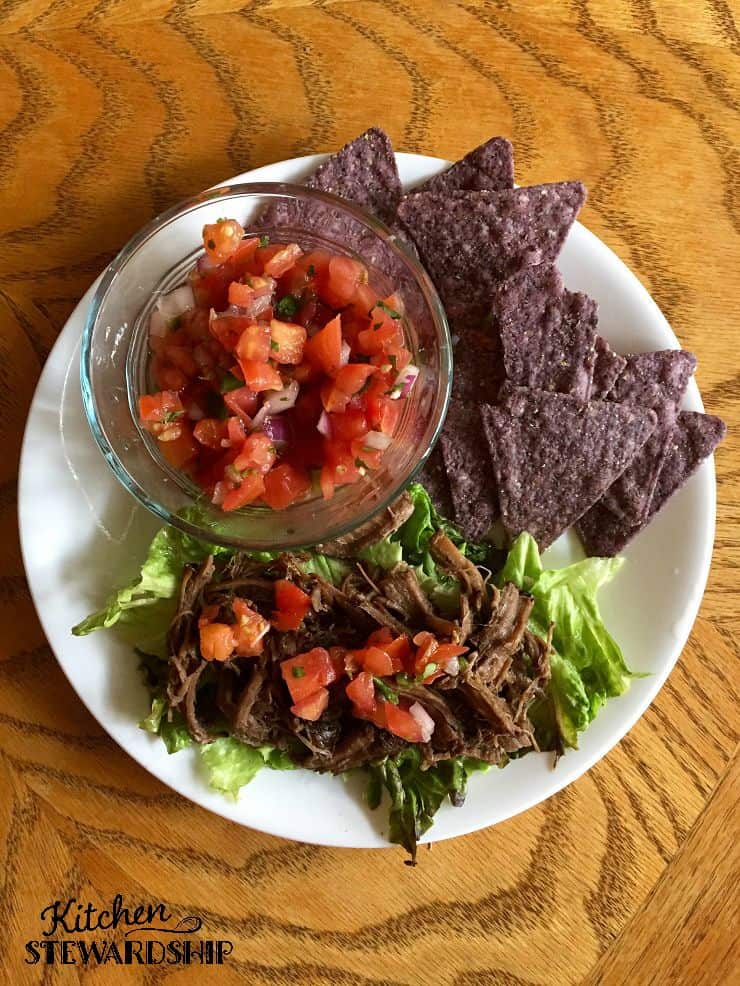 Instant Pot Barbacoa Beef served on lettuce with a side of chips and salsa.