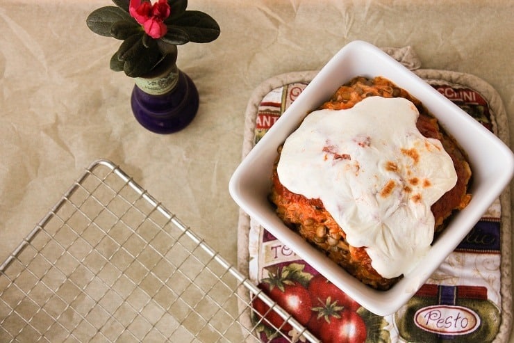 A bowl of instant pot Italian chicken and rice on a potholder with a small vase of flowers and a cooling rack. 