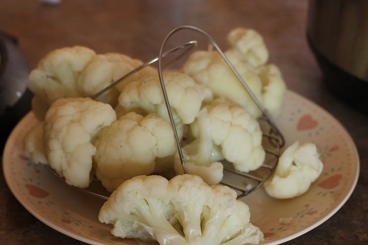 cooked cauliflower on an Instant Pot steaming insert lowered onto a dinner plate