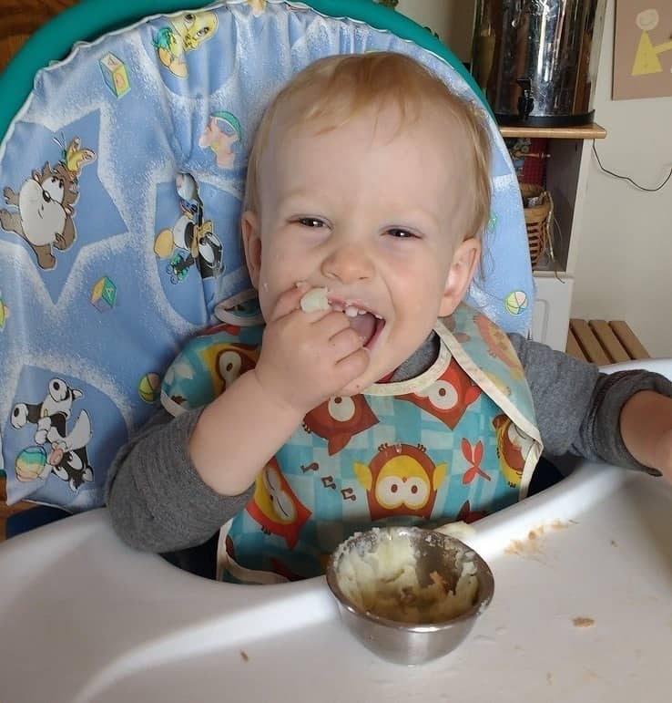 older baby eating mashed potatoes in the high chair