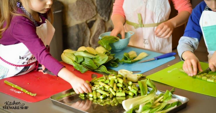 Young kids chopping asparagus and bok choy for an easy sheet pan dinner. 