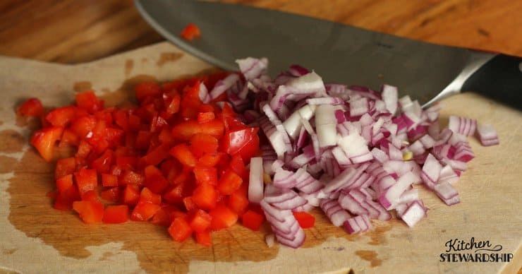 Chopped red pepper and red onion on a wood cutting board with a knife. Prepping veggies for brown rice, Mexican style, in the pressure cooker.