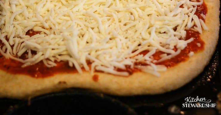 Uncooked whole wheat pizza dough topped with pizza sauce and shredded mozzarella cheese. 