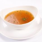 Homemade chicken stock in a white bowl on a white plate