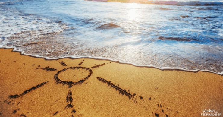 sun drawn in sand next to ocean waves