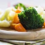 steamed vegetables - broccoli, cauliflower, and carrots - on a circular wooden plate