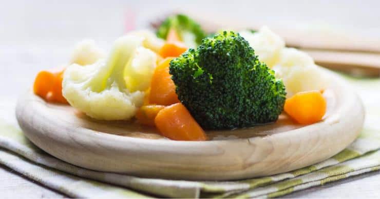 steamed vegetables - broccoli, cauliflower, and carrots - on a circular wooden plate