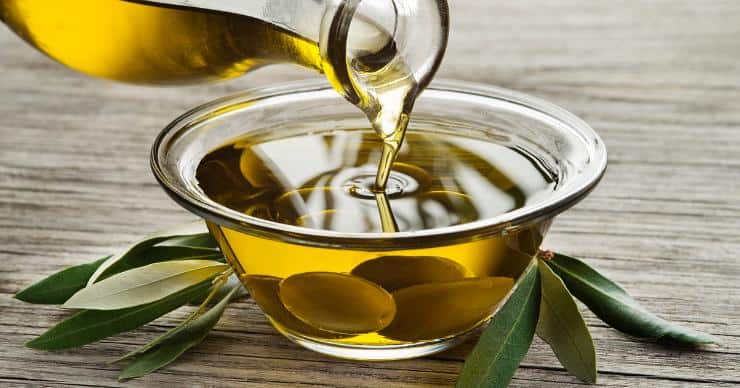 Bottle pouring olive oil into a bowl with olives
