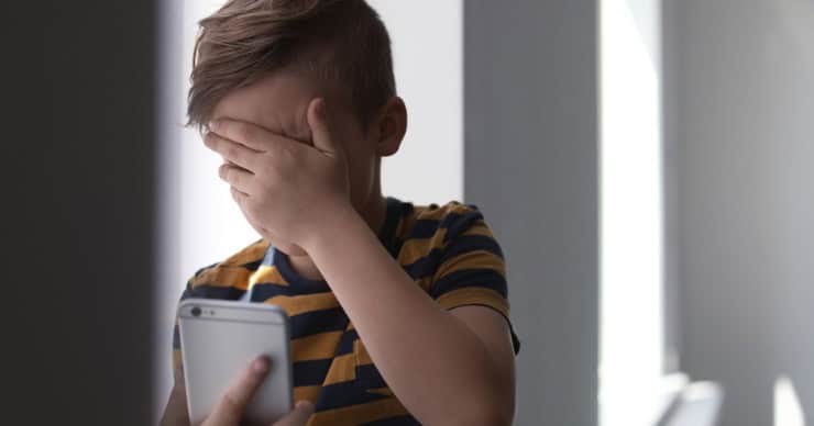 Boy covering his eyes watching phone